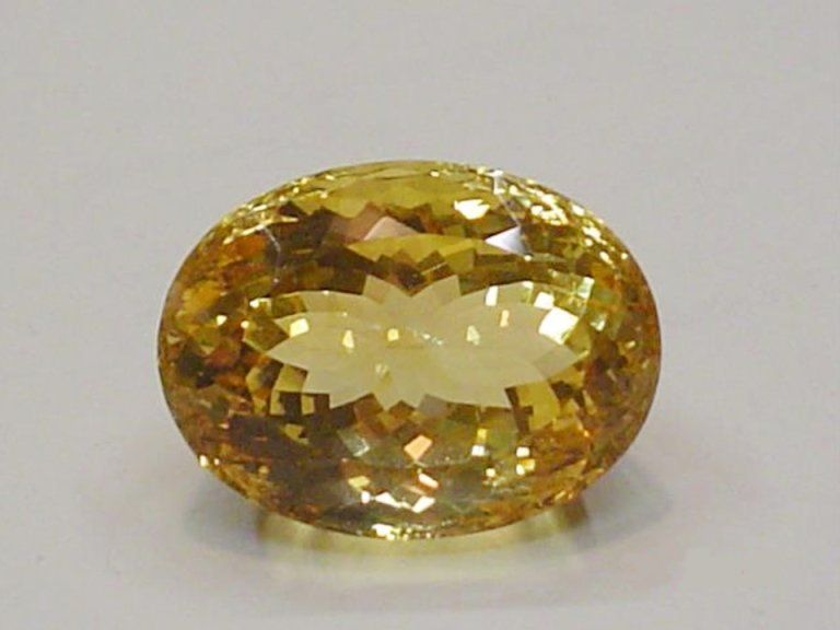 Una gemma di citrino giallo sfaccettata, dal taglio ovale, poggiata su una superficie bianca liscia.