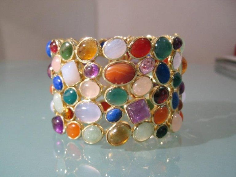 Un bracciale rigido a più fili con numerosi cabochon di pietre preziose lisce e colorate incastonati in metallo color oro.