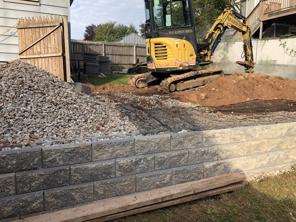 A yellow excavator is sitting on top of a pile of rocks.
