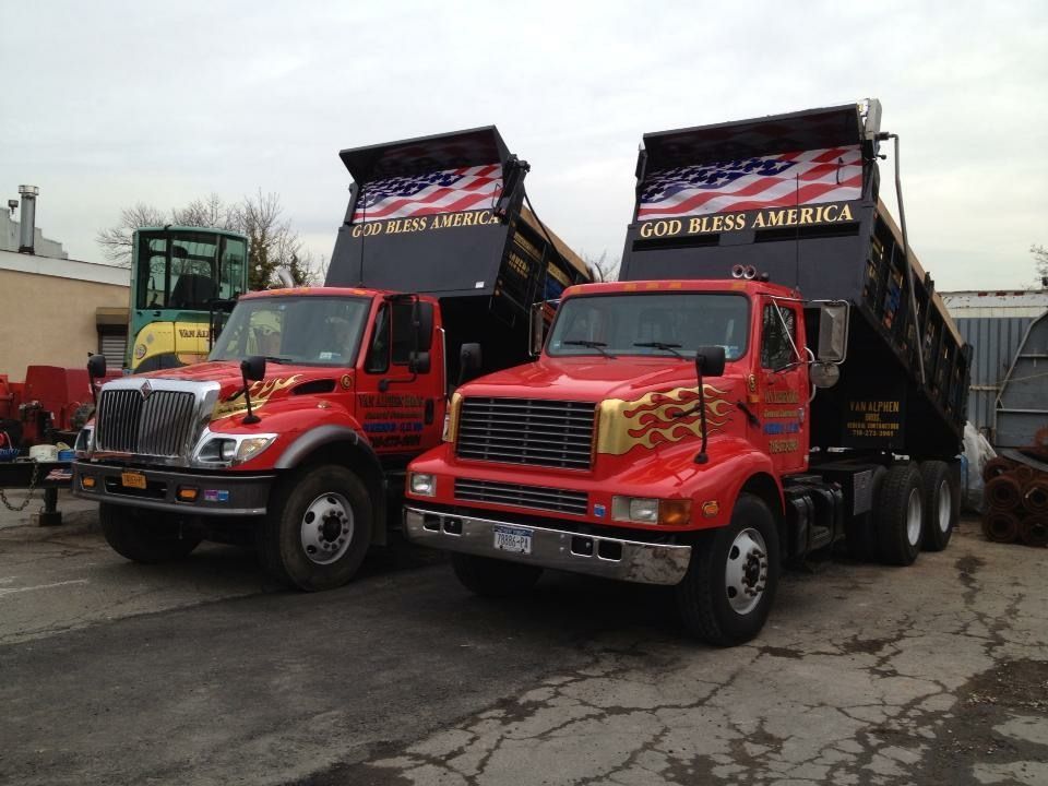 Two dump trucks are parked next to each other with one saying give us america