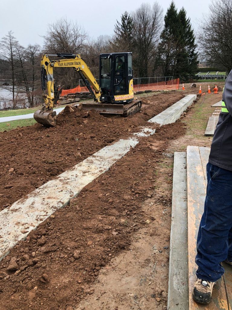 A man is standing next to a yellow excavator in a dirt field.
