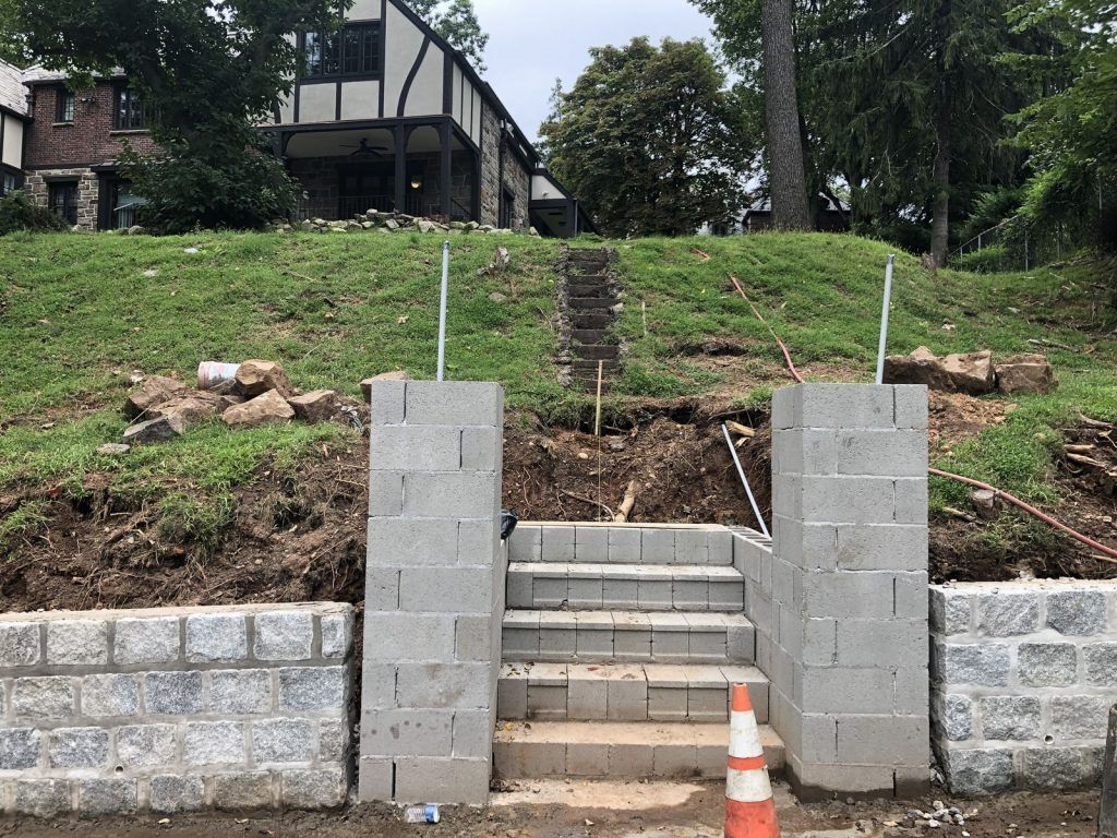 A brick wall with stairs leading up to a house in the background.