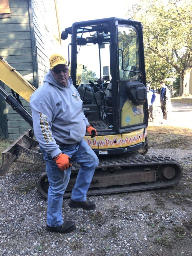A man is standing next to a small excavator.