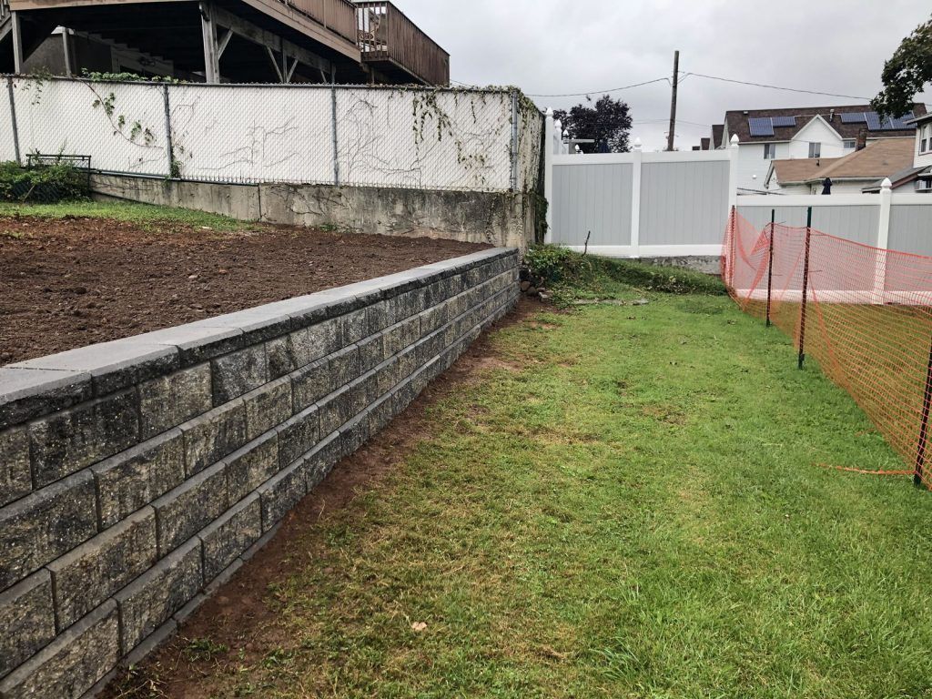 A brick wall surrounds a lush green field with a white fence in the background.