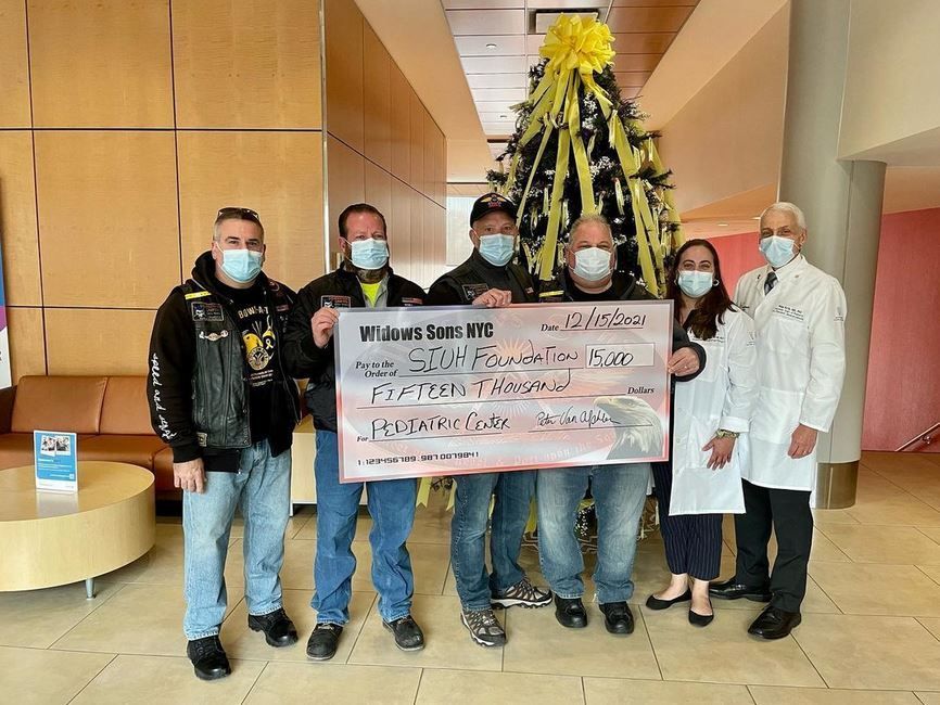 A group of people holding a large check in front of a christmas tree