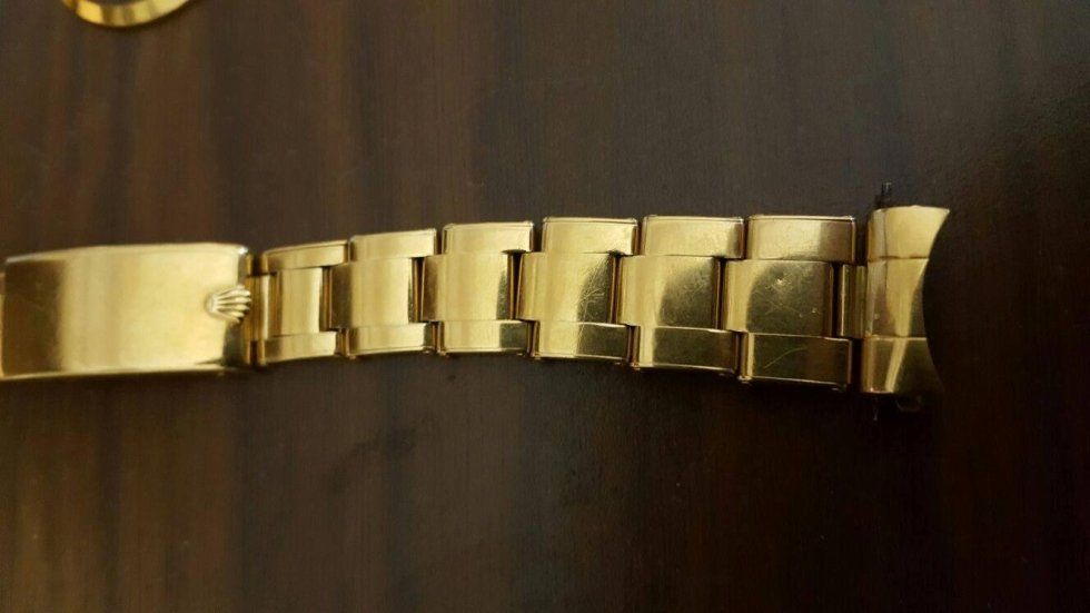 Un cinturino d'oro è appoggiato su un tavolo di legno.