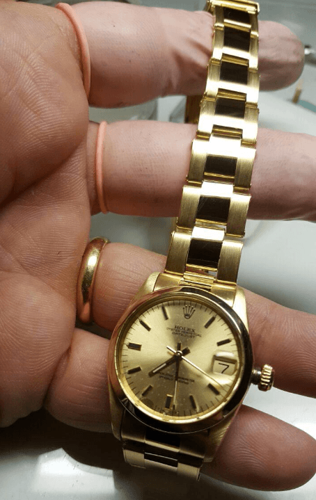 Una persona tiene un orologio Rolex d'oro tra le dita