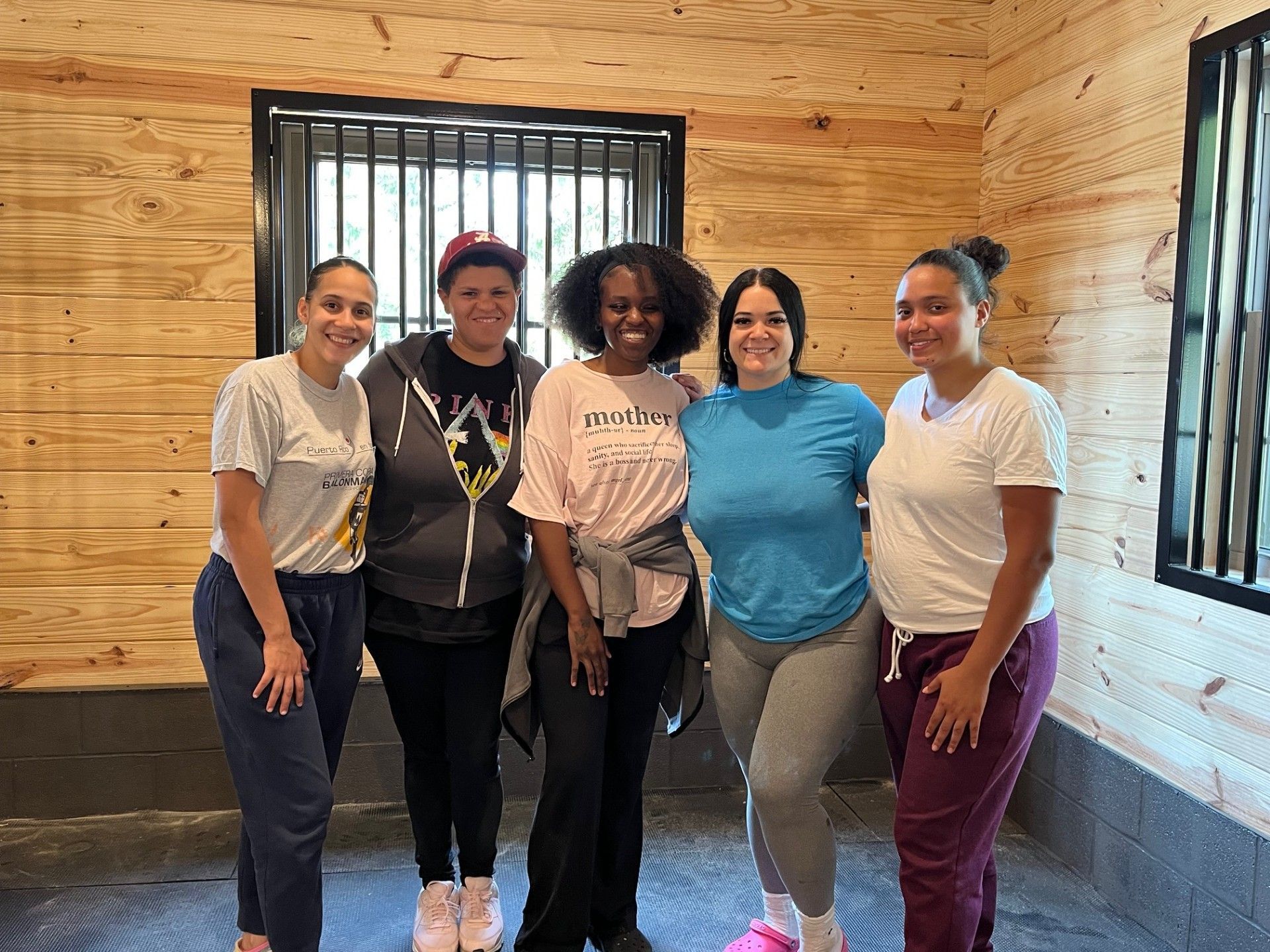 Five people smiling in a barn with wood paneling. They are in casual clothing.