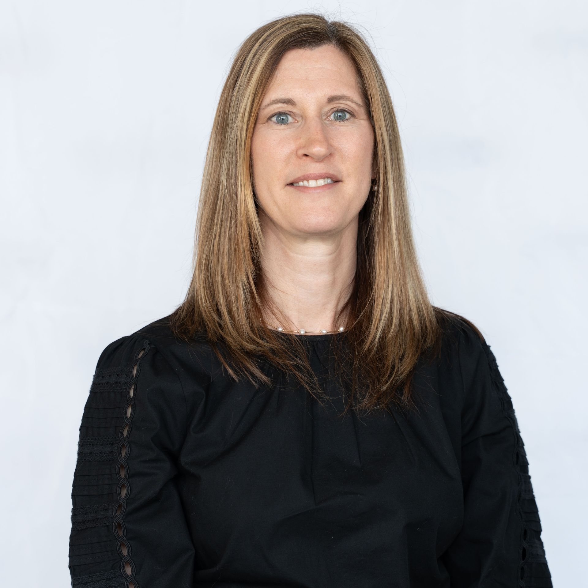 Woman with light brown hair in a black top smiles against a white background.