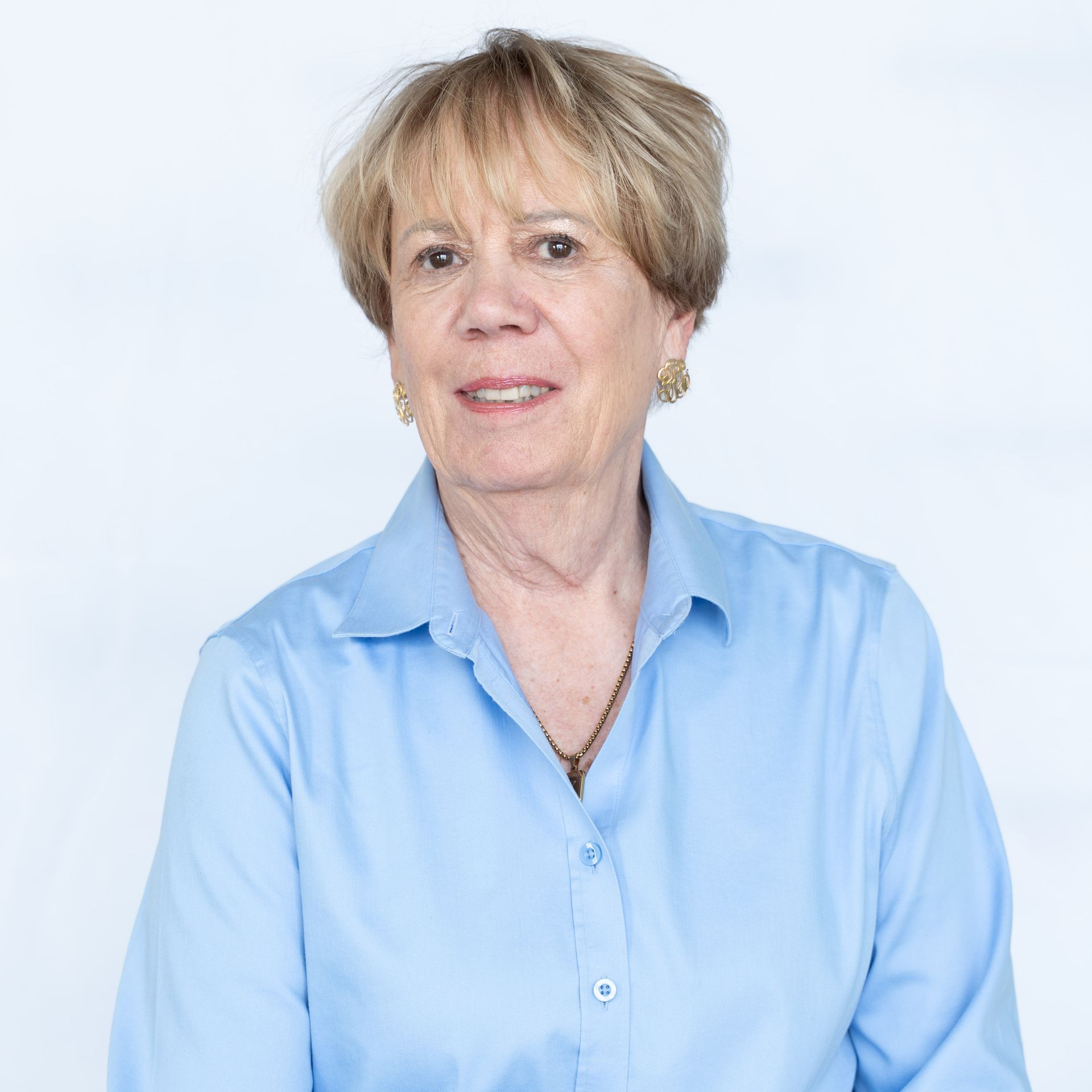 Woman with short blonde hair wearing a blue button-down shirt smiles against a white background.