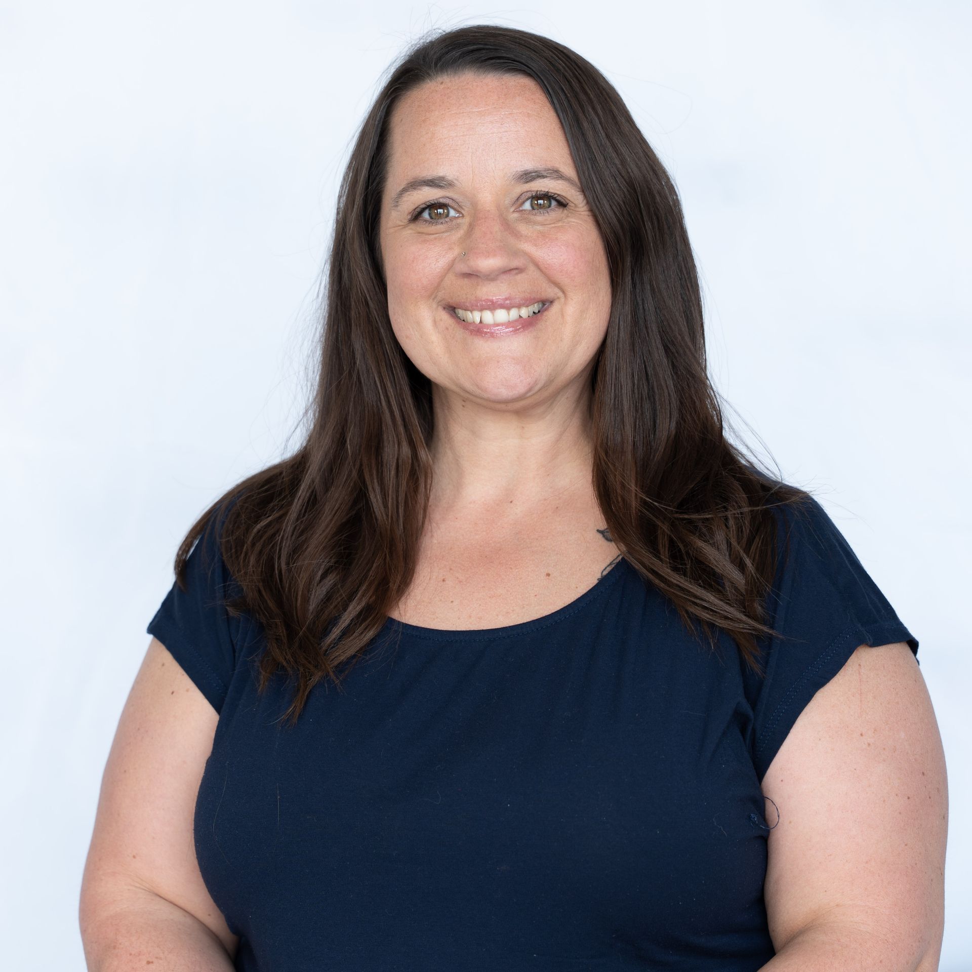 Woman with long brown hair smiles, wearing a dark blue shirt against a white backdrop.