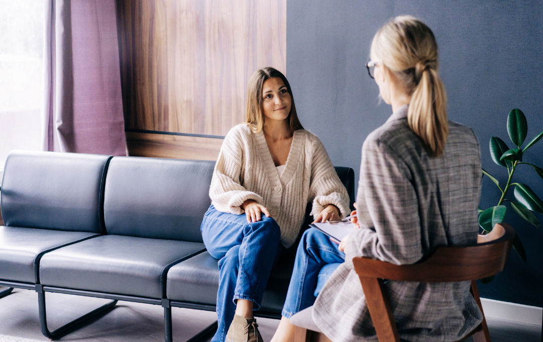 Woman on couch talking to person in chair, in a consultation room.