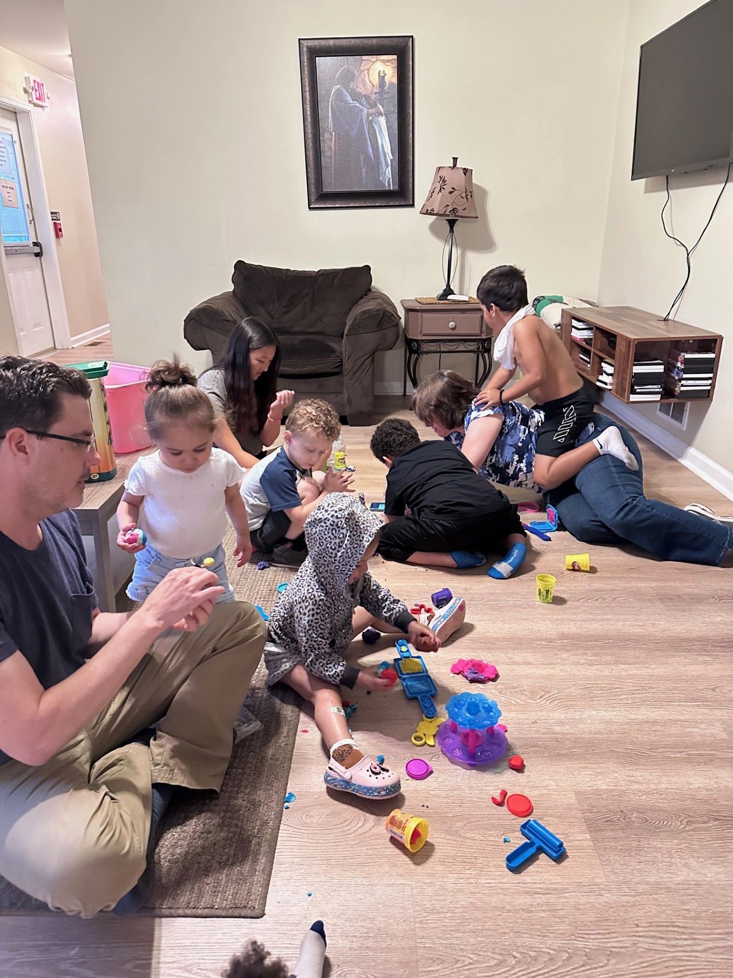 People playing with toys on a floor, adults nearby, in a living room.