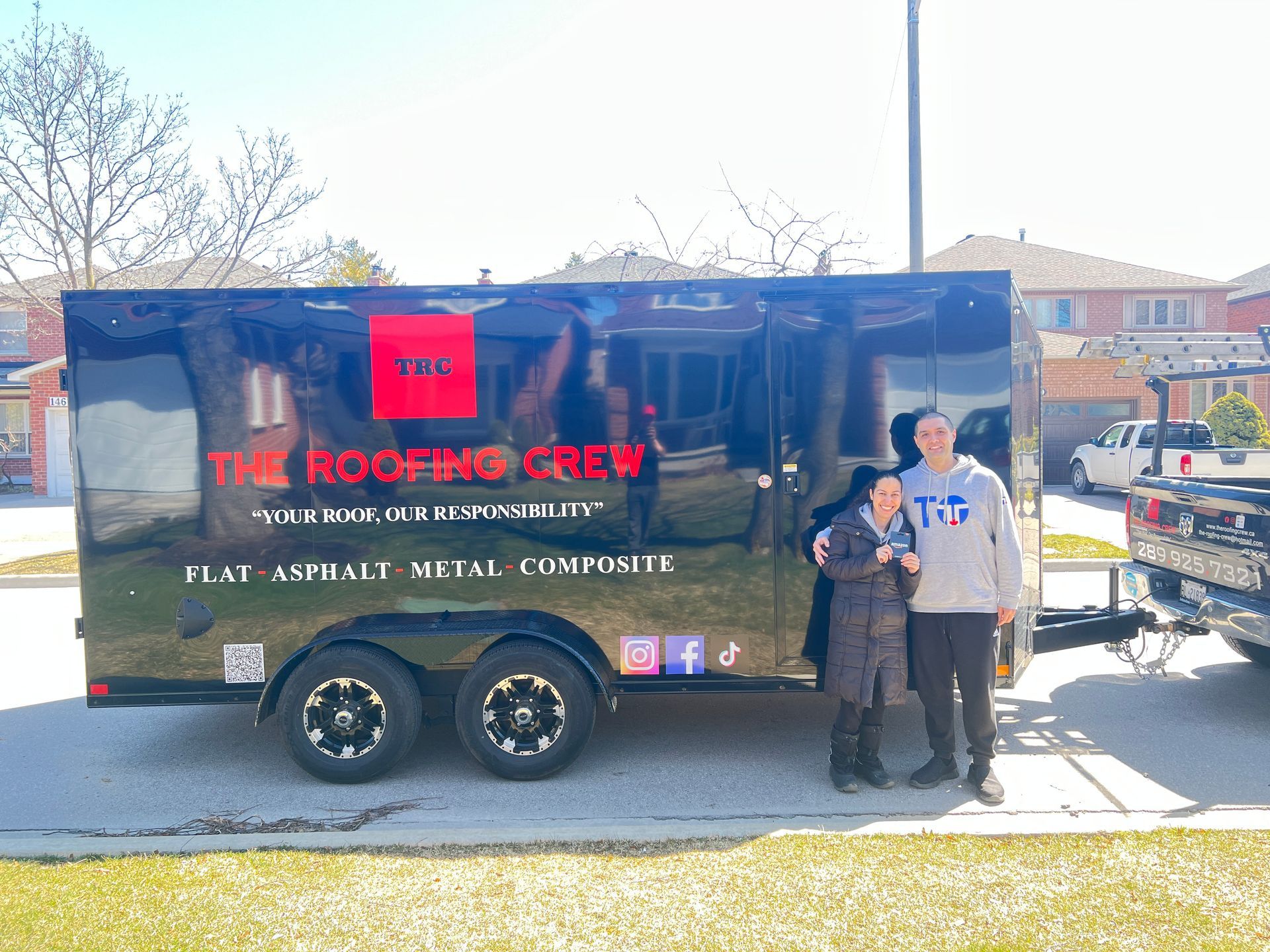 Two people standing in front of a trailer that says the roofing crew