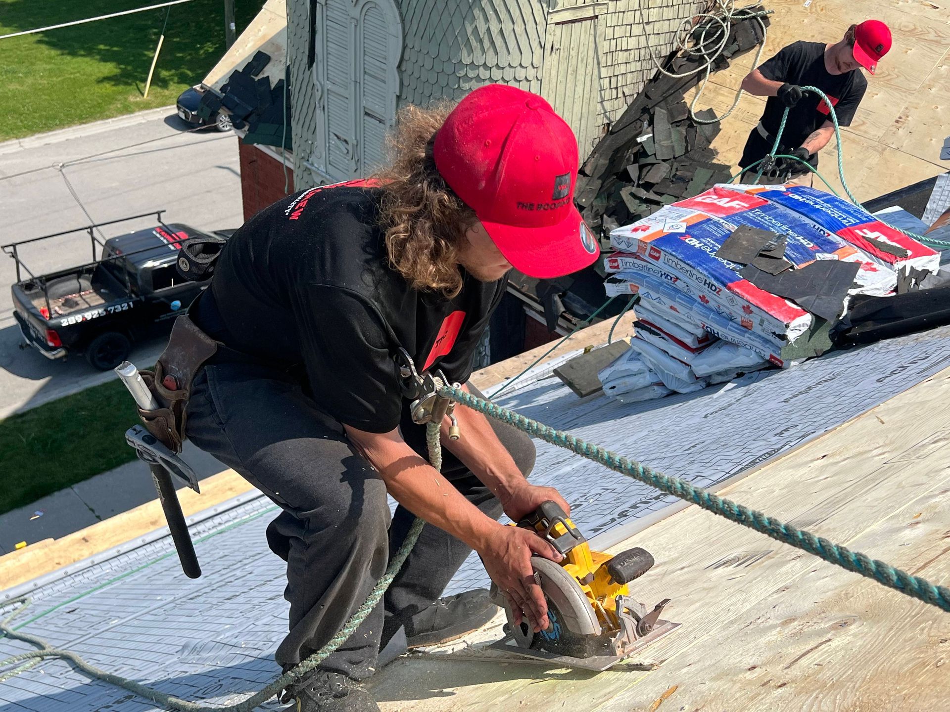 A man wearing a red hat is using a circular saw on a roof.