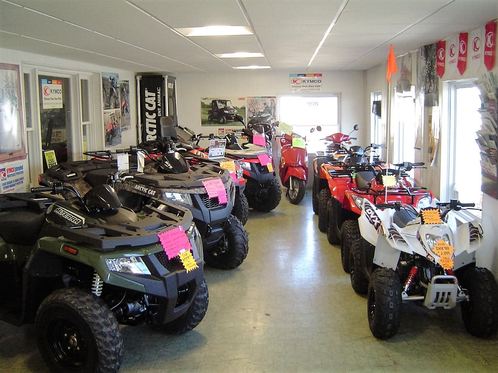 ATV and scooter showroom, vehicles on display with price tags. Interior shot.