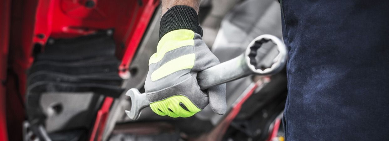 A mechanic wearing a glove holds a wrench while working on a red vehicle.
