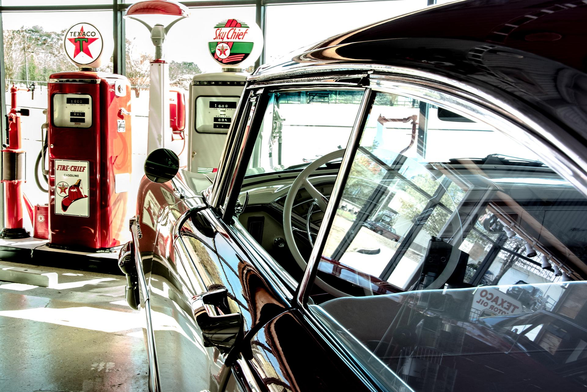 Classic black car parked at a retro gas station with red pumps and green signage.