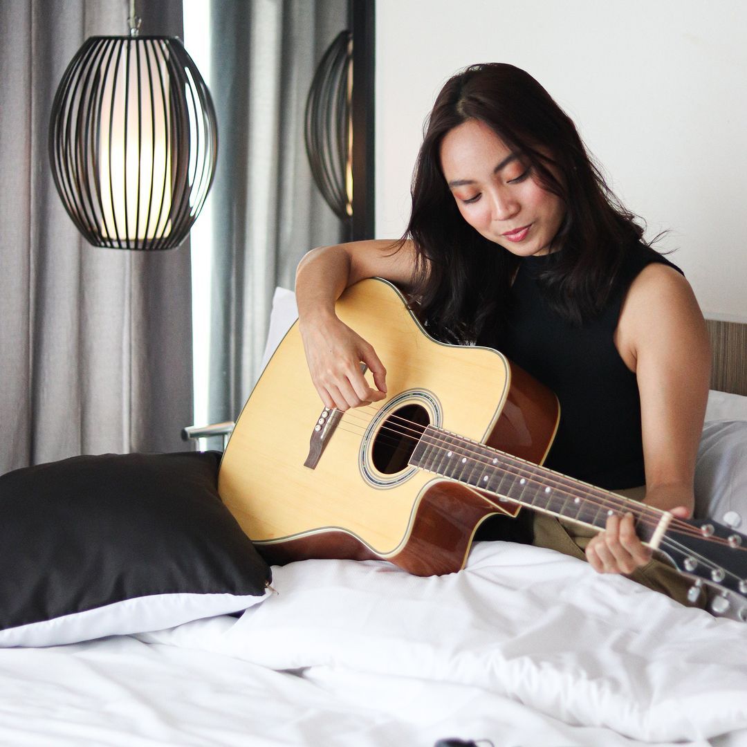 A woman playing an acoustic guitar and relaxing during her staycation in Makati