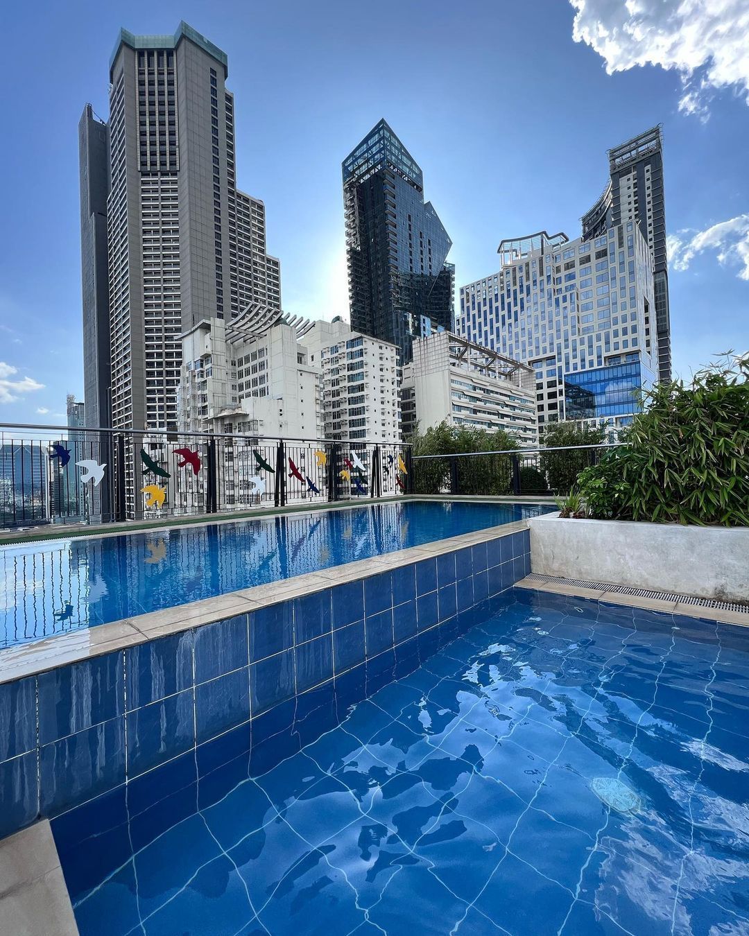 Rooftop pool with blue water and cityscape background, sunny day. Skyscrapers, clouds, and light blue sky.