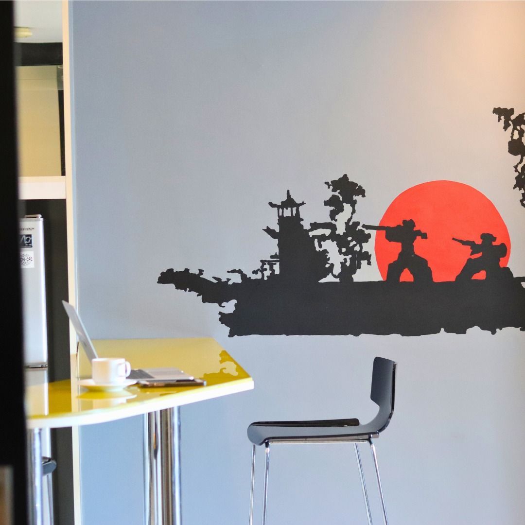 Yellow desk with laptop and coffee, black bar stool, Japanese-themed wall art with red sun and ninja silhouettes.