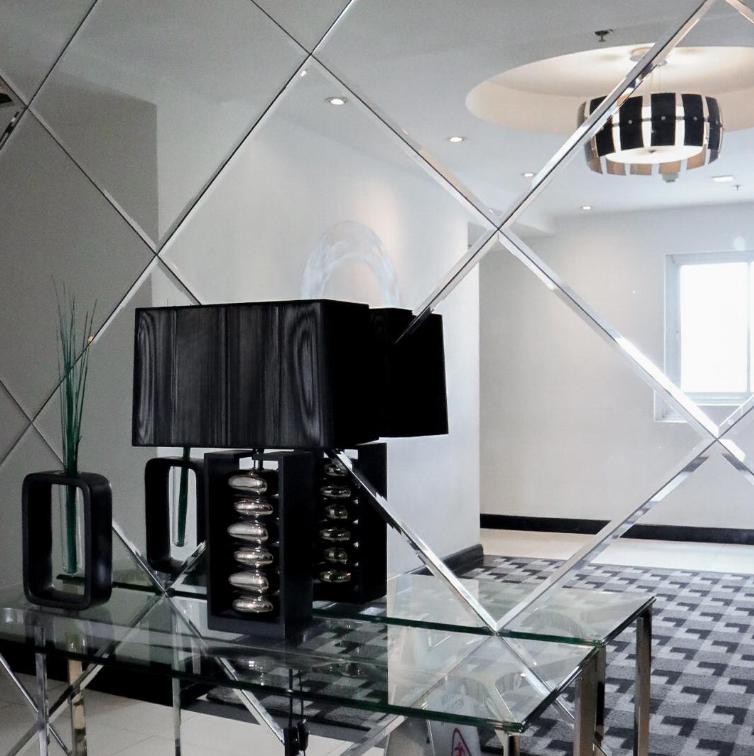 A black lamp sits on a glass table in front of a mirrored wall