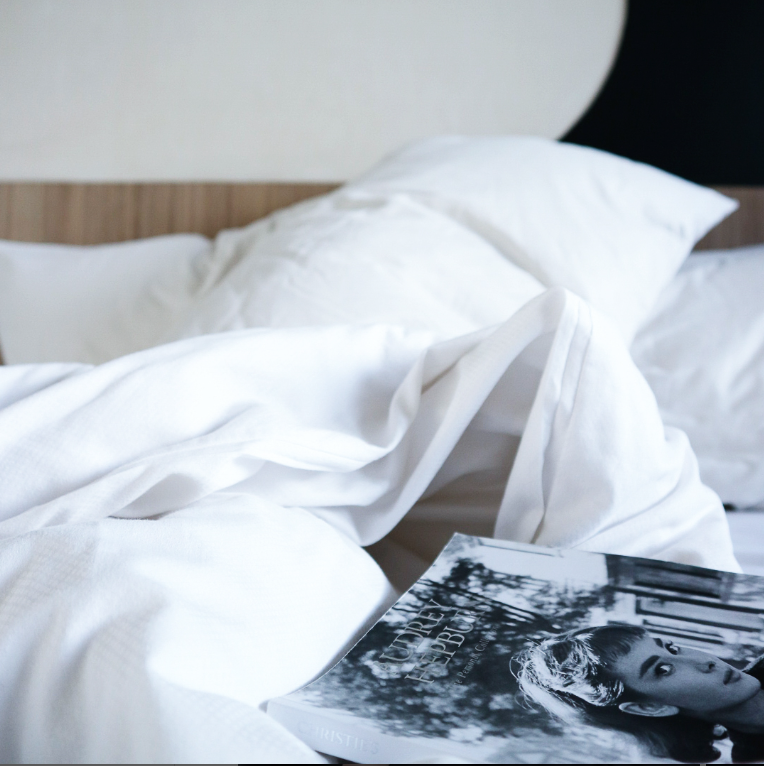 White bedding on a bed, with a magazine in the foreground and a wooden headboard.