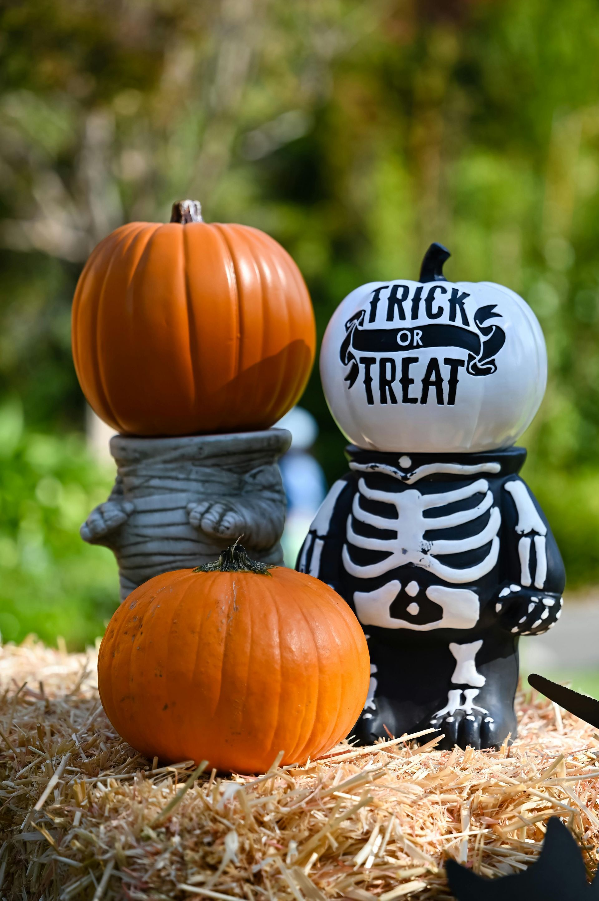 Halloween decorations: pumpkins and skeleton figures on a hay bale, outdoors.