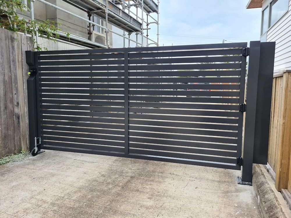 A Black Gate is Sitting on Top of a Concrete Driveway Next to a Wooden Fence —  SCF Industries Pty Ltd in Albion Park, NSW