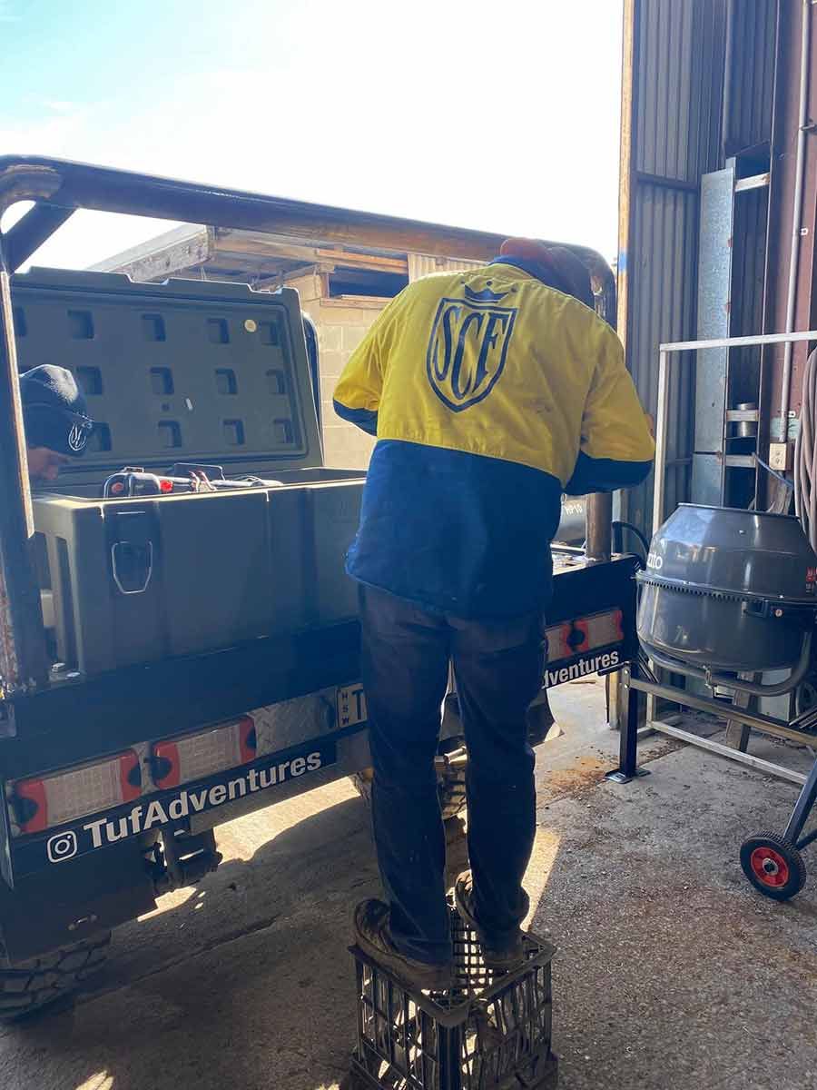 A Man in a Yellow and Blue Jacket is Standing on a Crate Next to a Truck —  SCF Industries Pty Ltd in Albion Park Rail, NSW