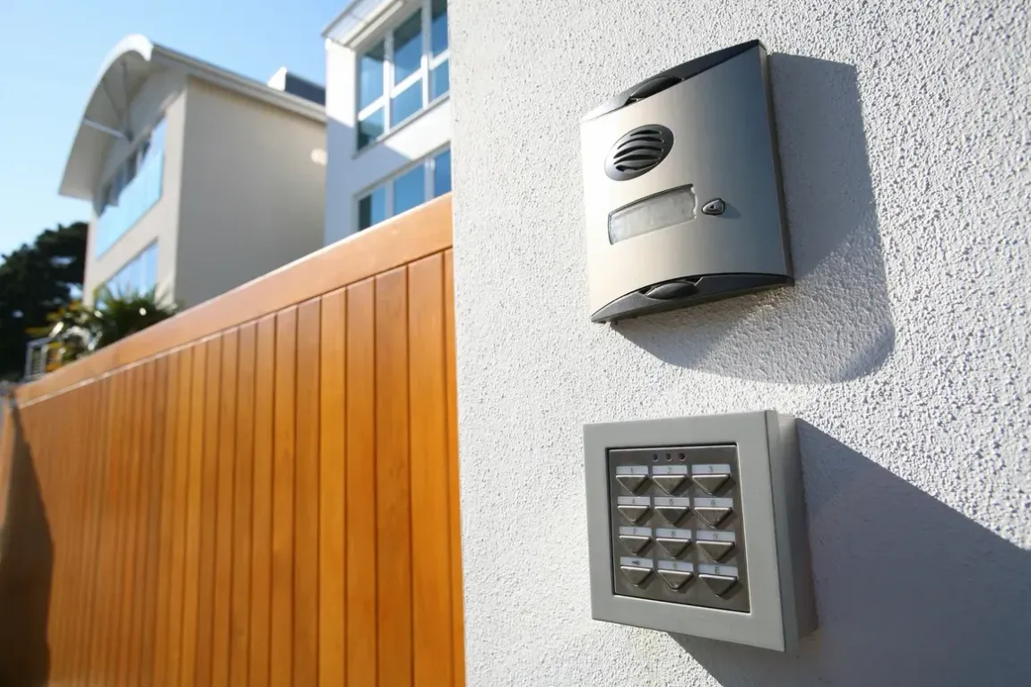 A white wall with a wooden fence and a doorbell on it