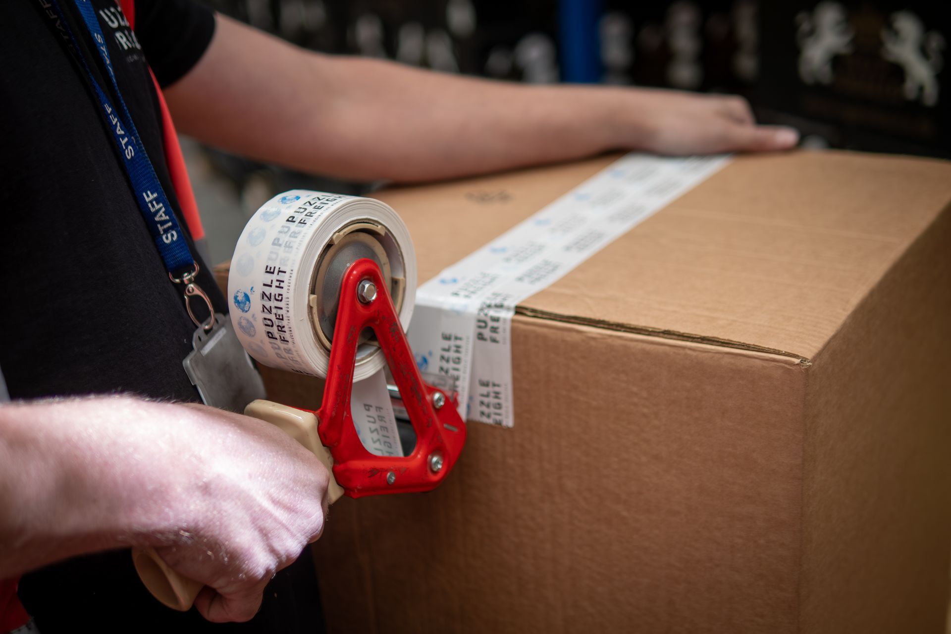 Person taping a cardboard box with a tape dispenser, likely in a warehouse setting.