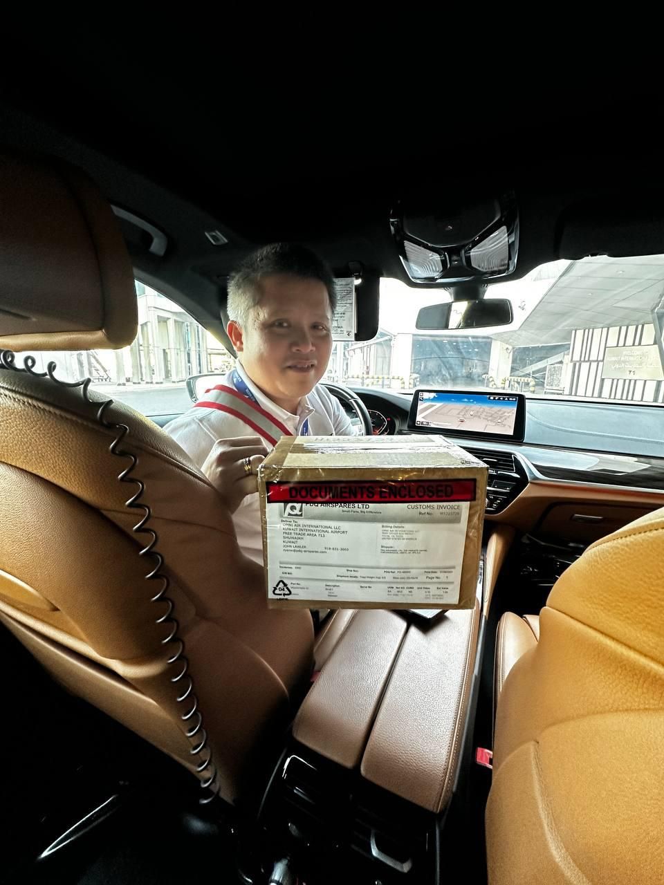 Person in a car holding a cardboard box. Tan interior. The person smiles.