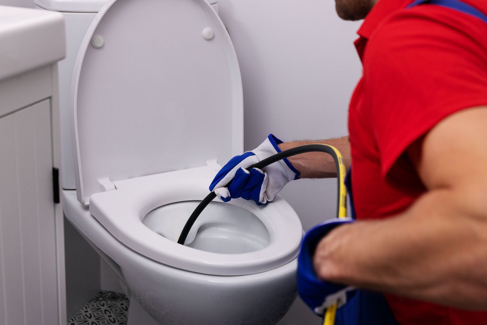 A man is cleaning a toilet with a hose.