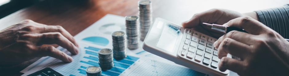 A person is using a calculator in front of stacks of coins.