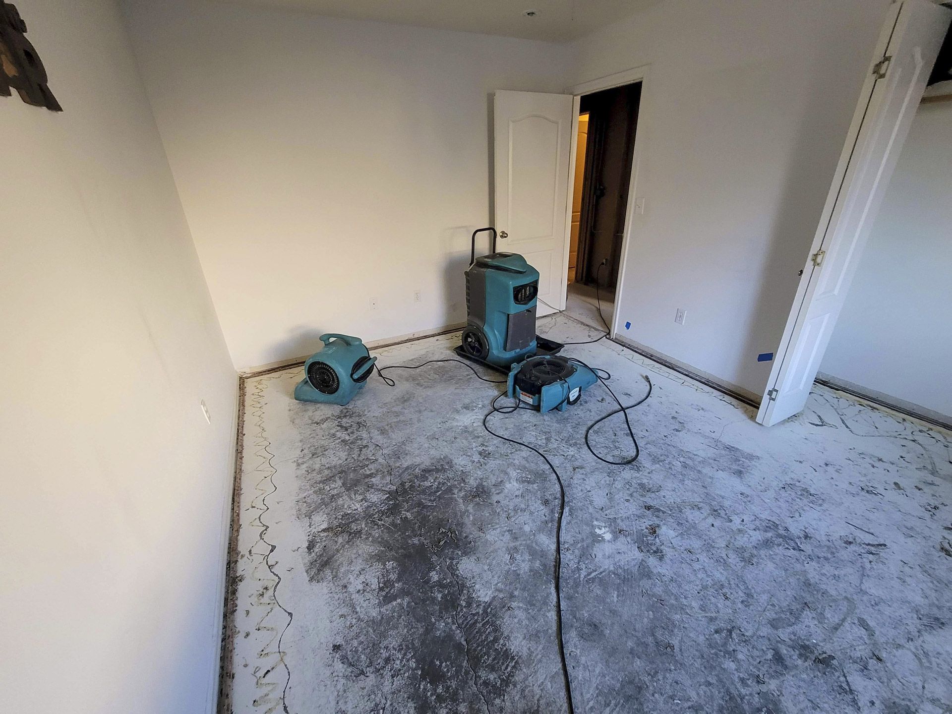 A water-damaged bedroom with carpet removed and air movers with a dehumidifier for drying