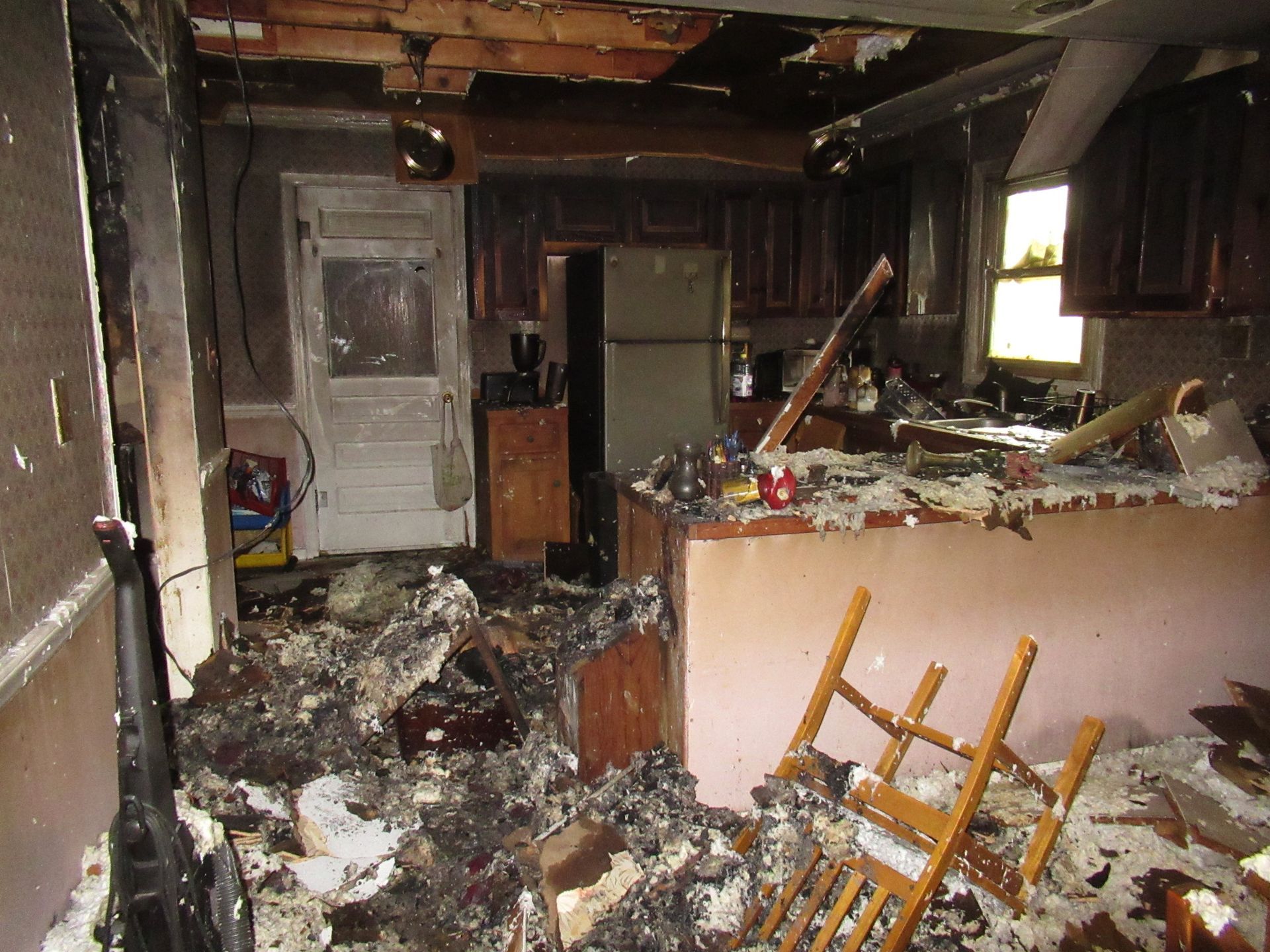 Interior of a kitchen destroyed by fire; debris, charred cabinets, and a damaged ceiling are visible.