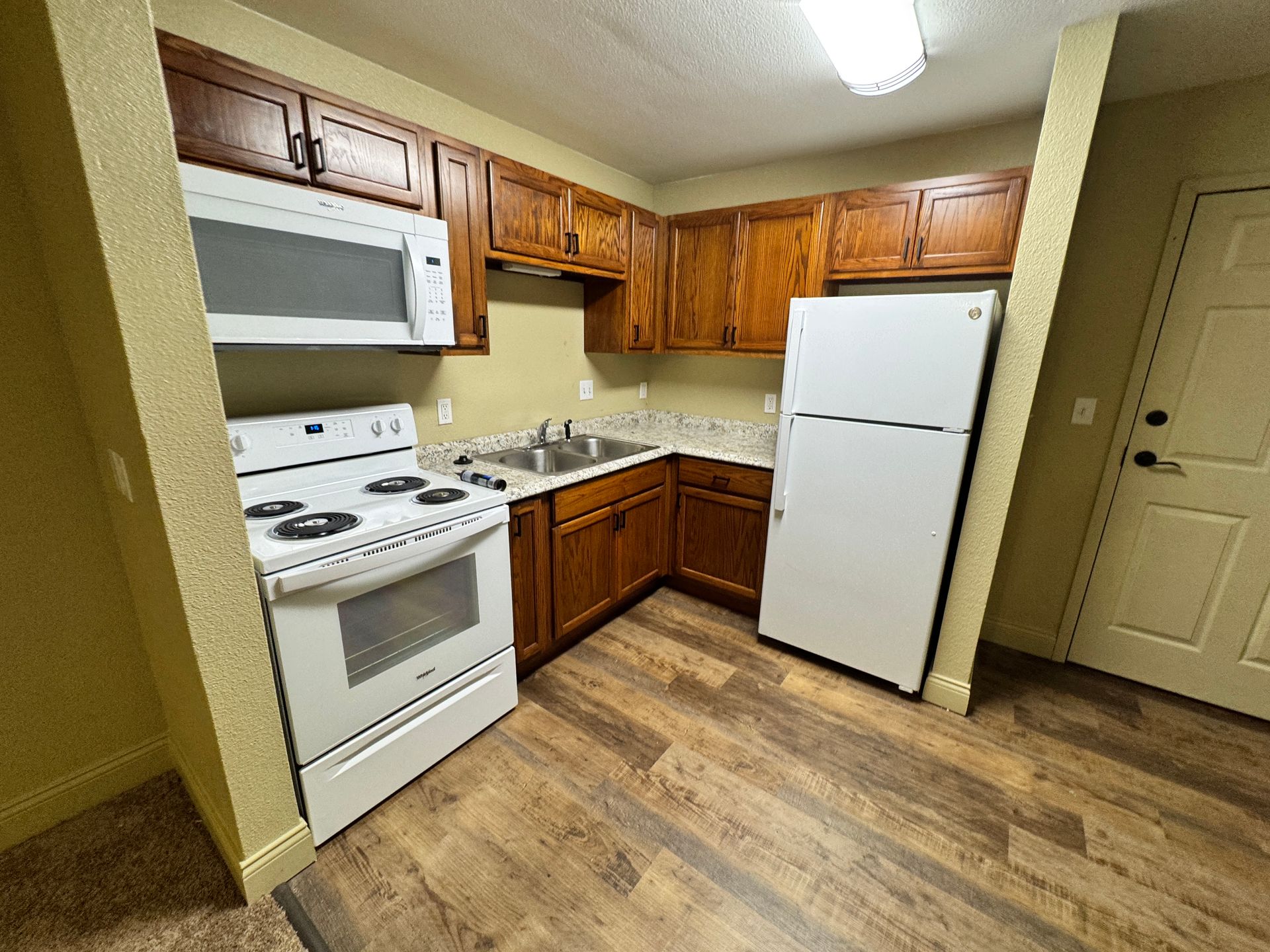 Small kitchen with brown cabinets, white appliances, and wood-look flooring.