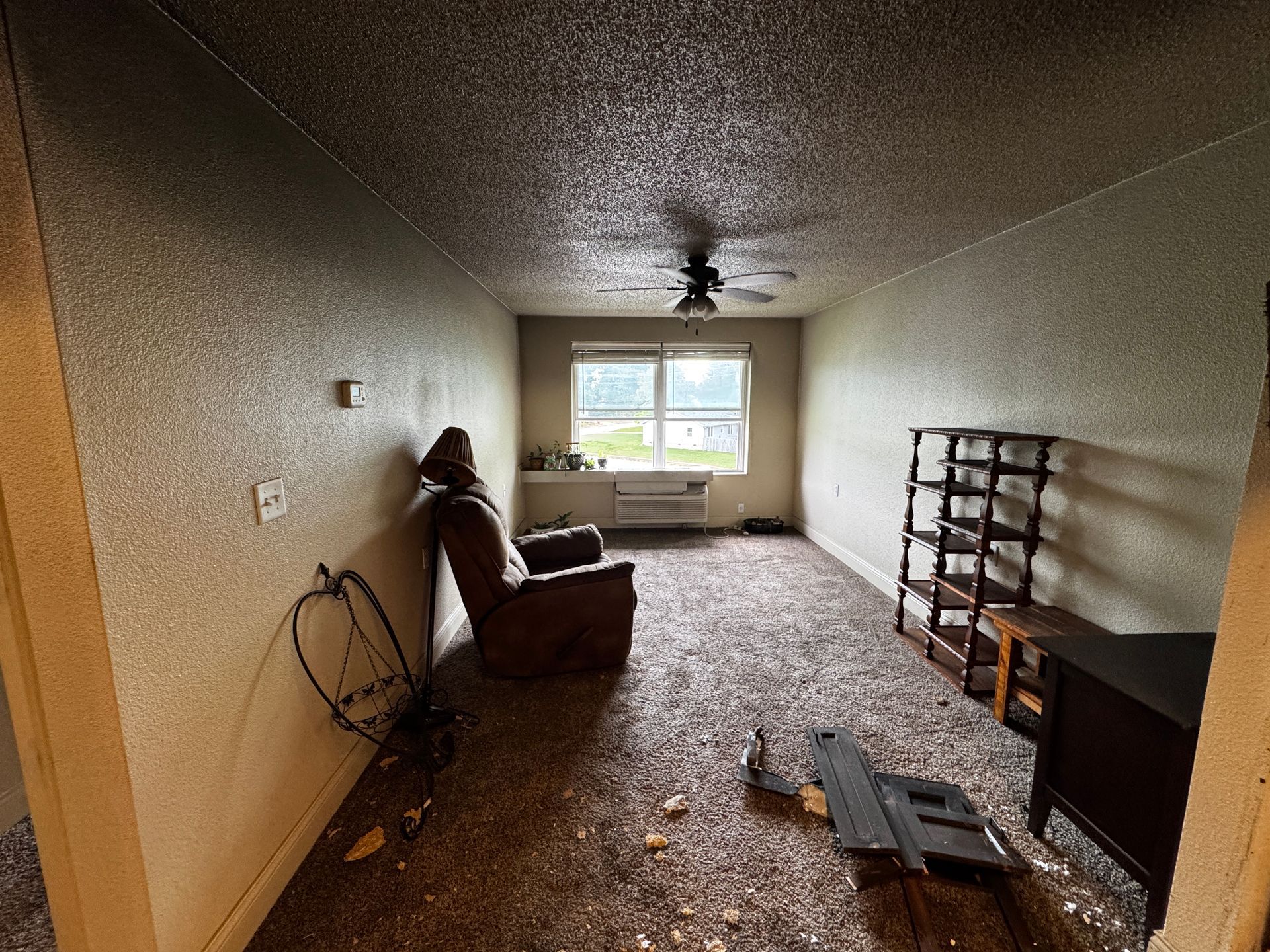 Interior of a room with water damage. Brown recliner, shelves, ceiling fan. Flooded floor.