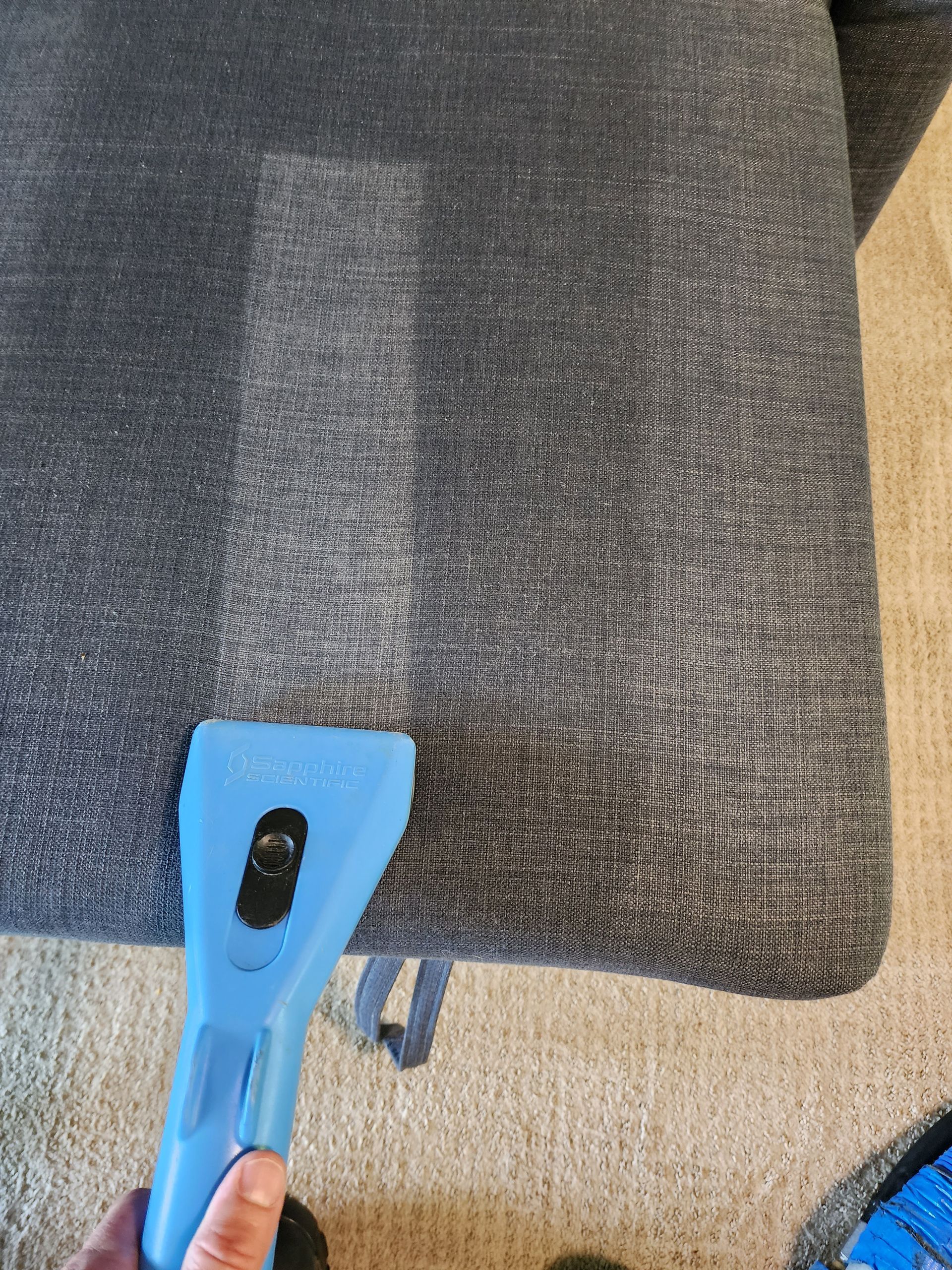 A person is cleaning a couch with a vacuum cleaner.