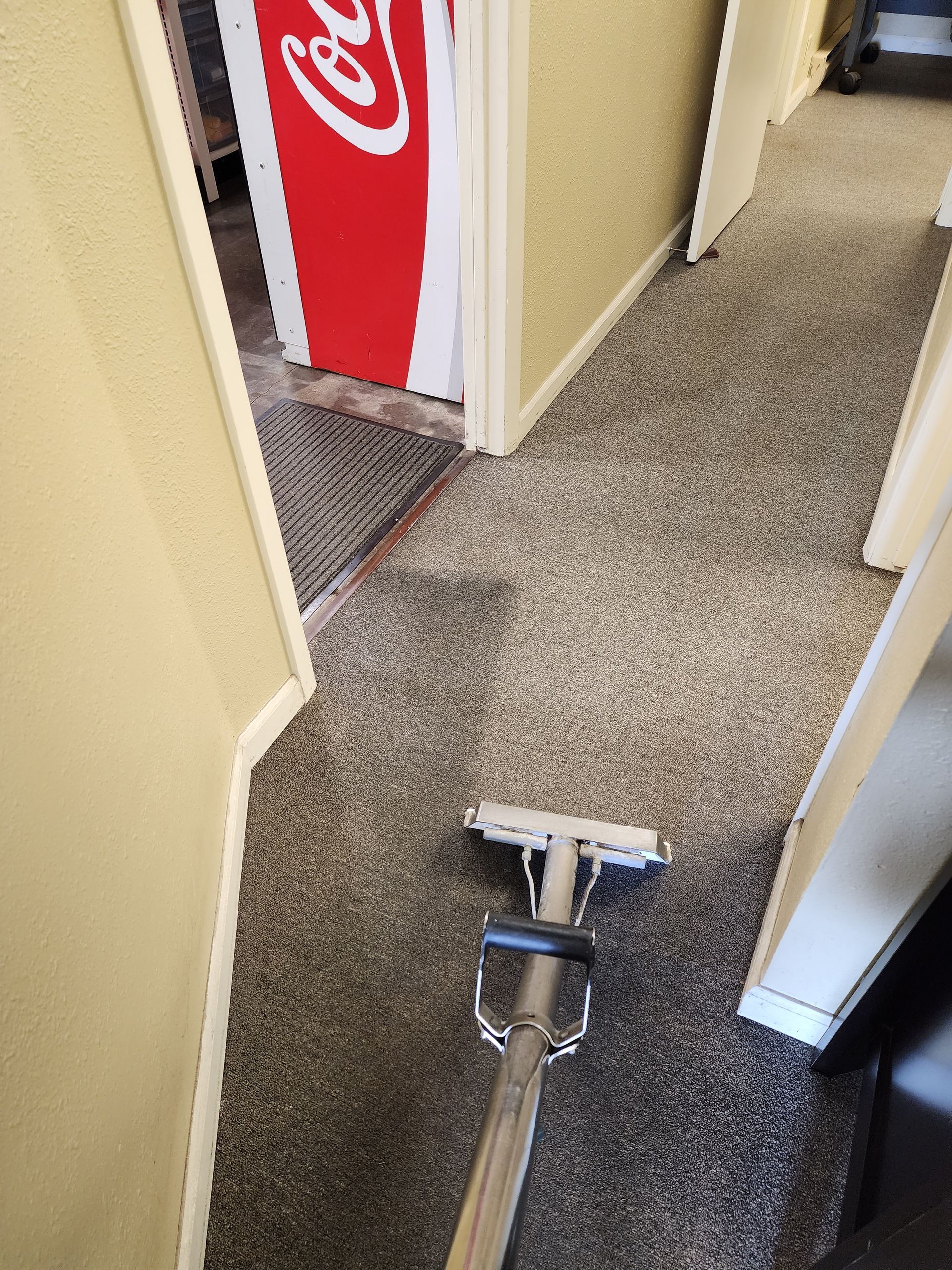 A vacuum cleaner is cleaning a carpet in a hallway.