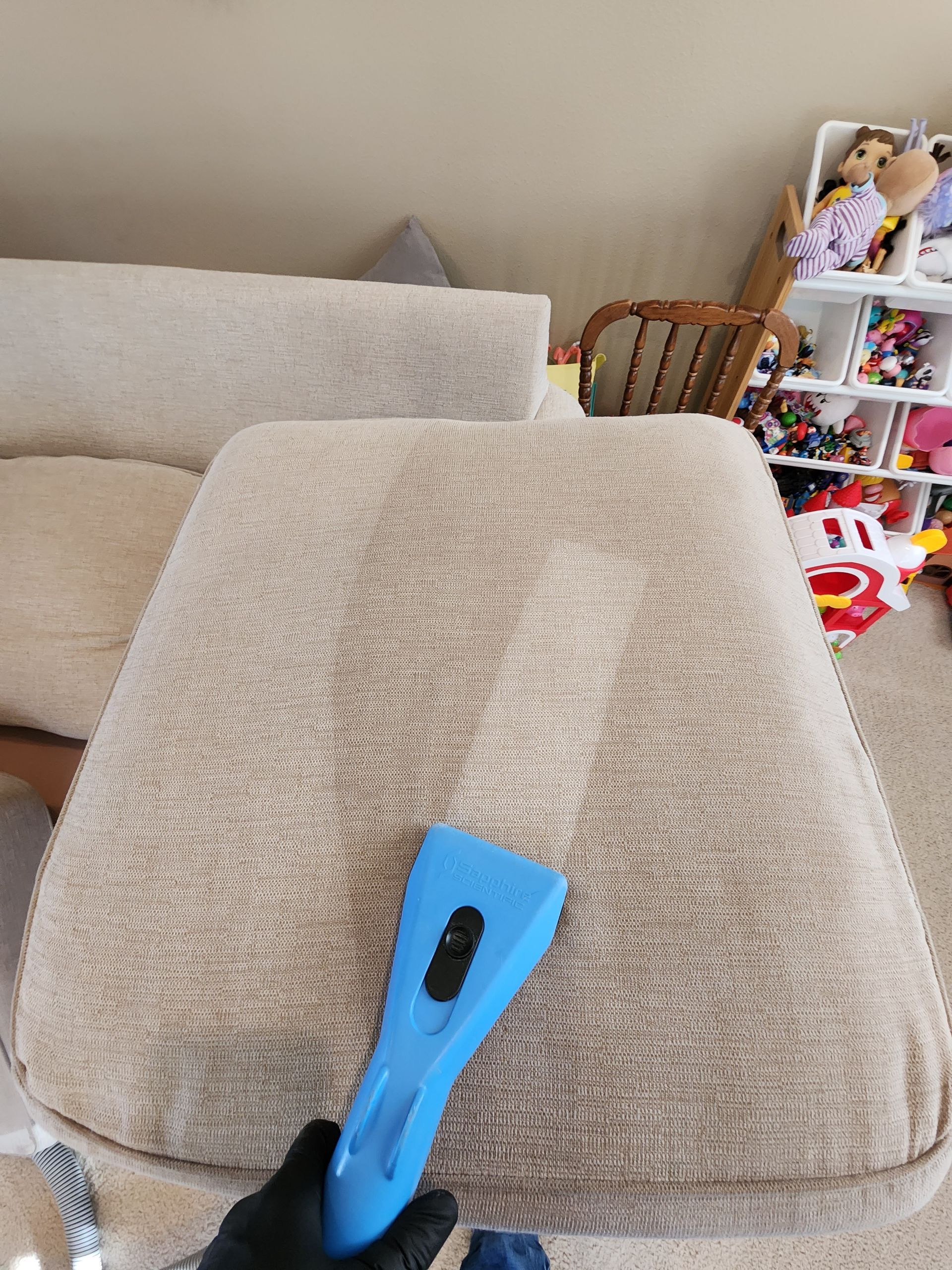 A person is cleaning a couch with a vacuum cleaner.