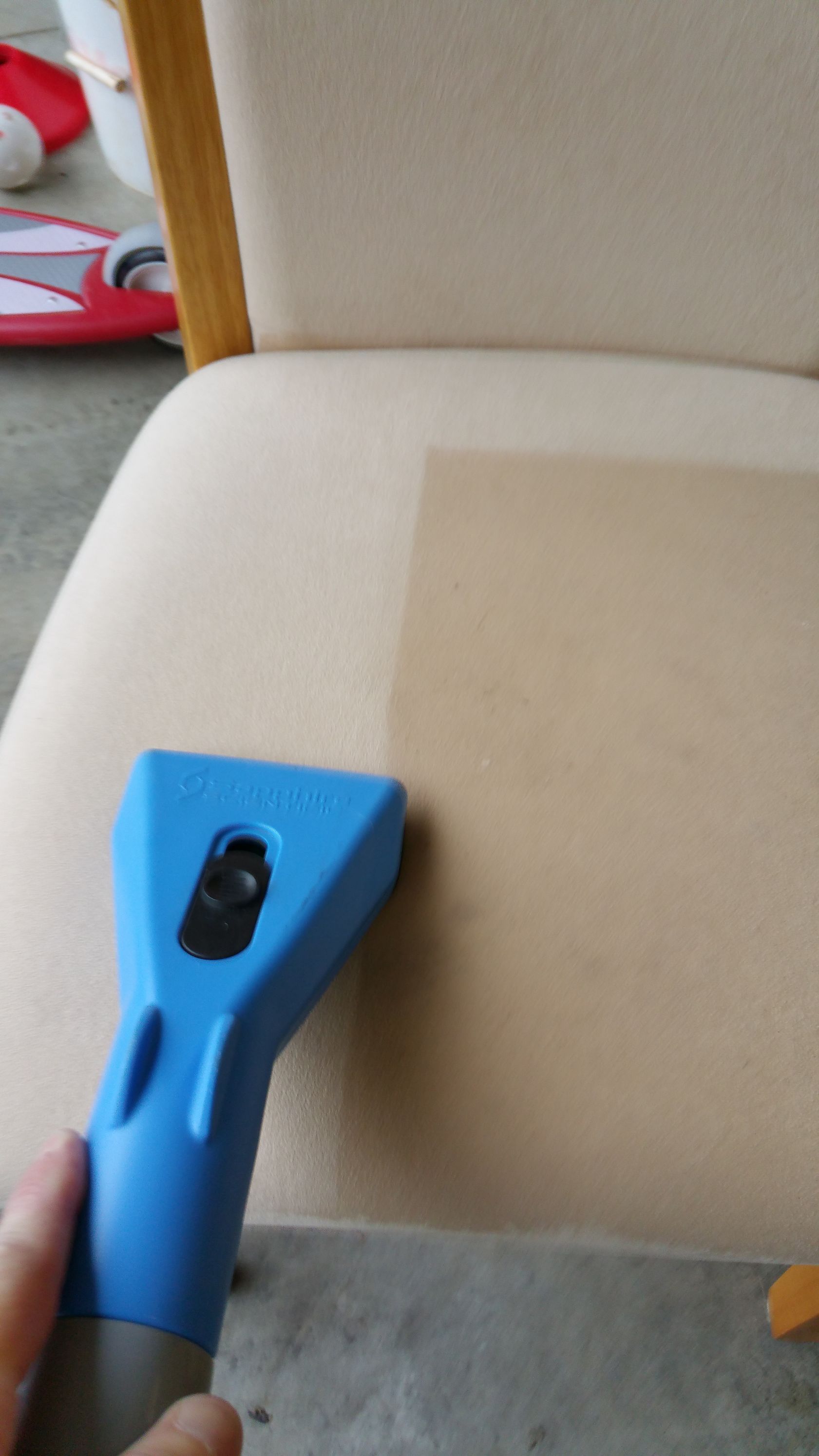 A person is cleaning a chair with a blue vacuum cleaner.