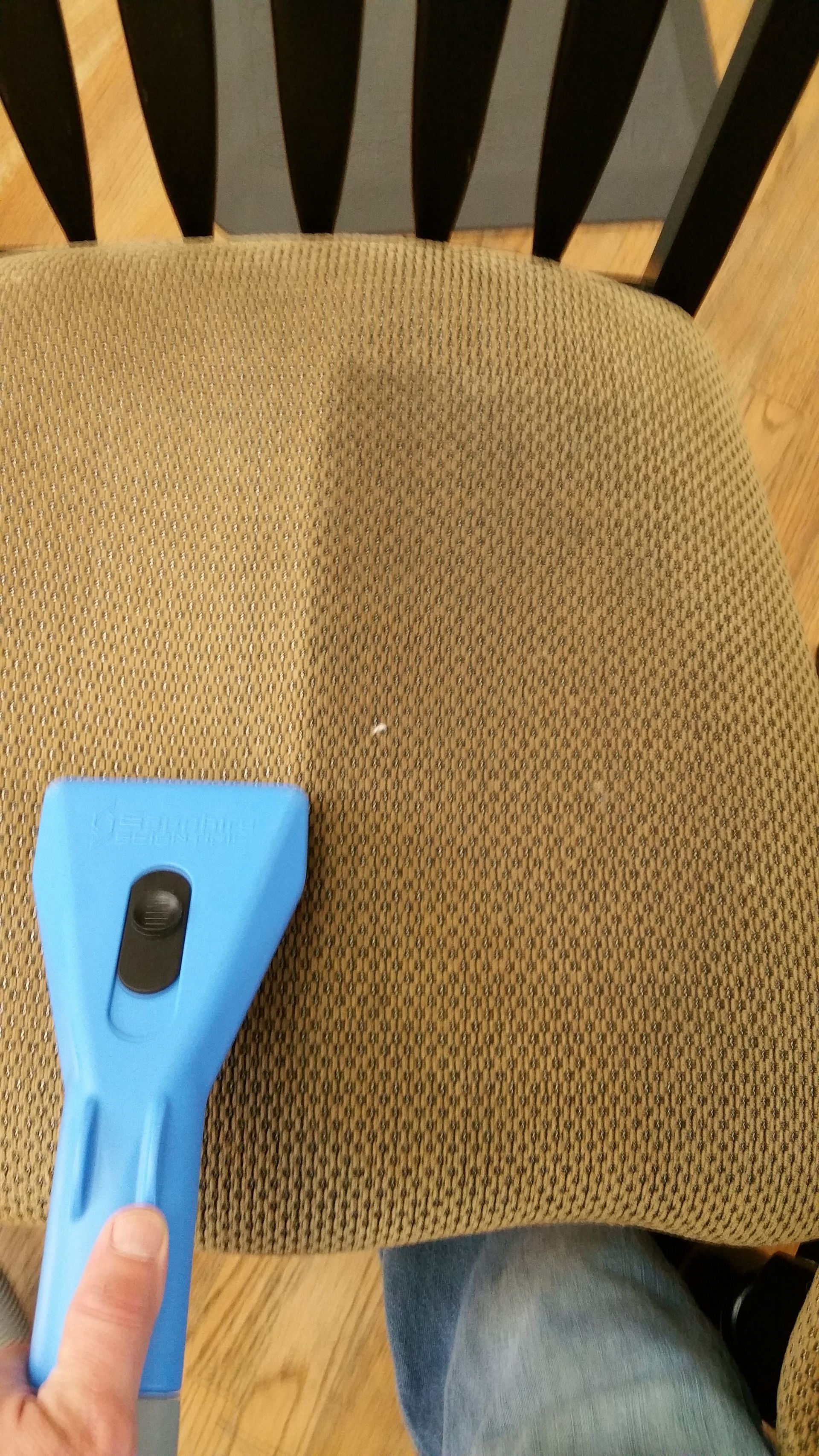 A person is cleaning a chair with a blue vacuum cleaner.