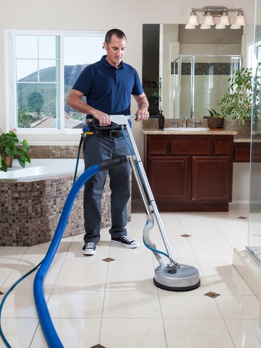 A man is cleaning a bathroom floor with a vacuum cleaner.