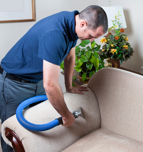 A man is cleaning a couch with a vacuum cleaner
