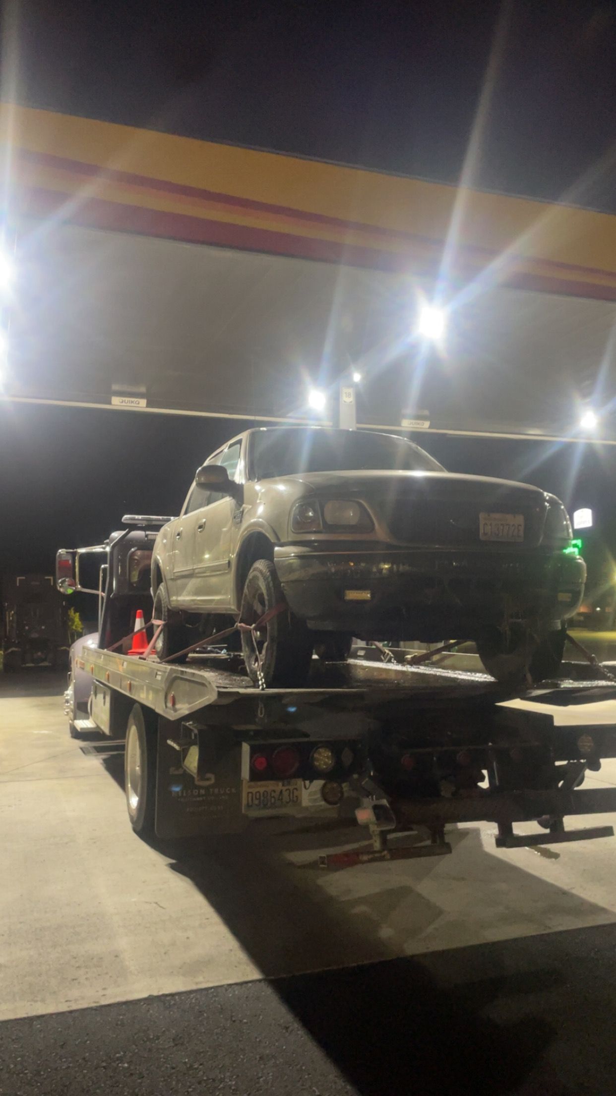 Car carrier trailer loaded with a car at a gas station at night under bright lights