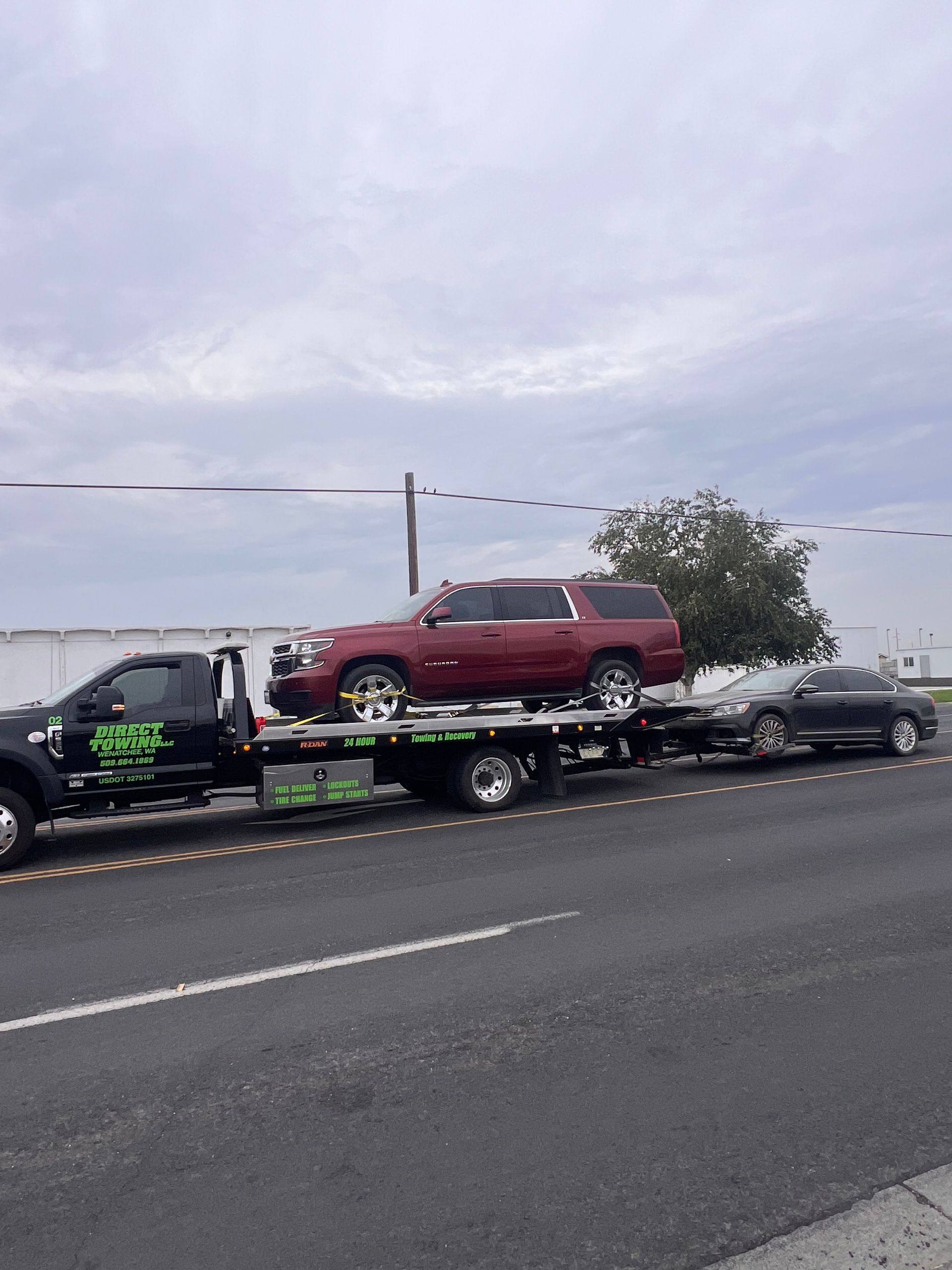 Tow truck hauling a red SUV on a flatbed beside a highway under cloudy skies