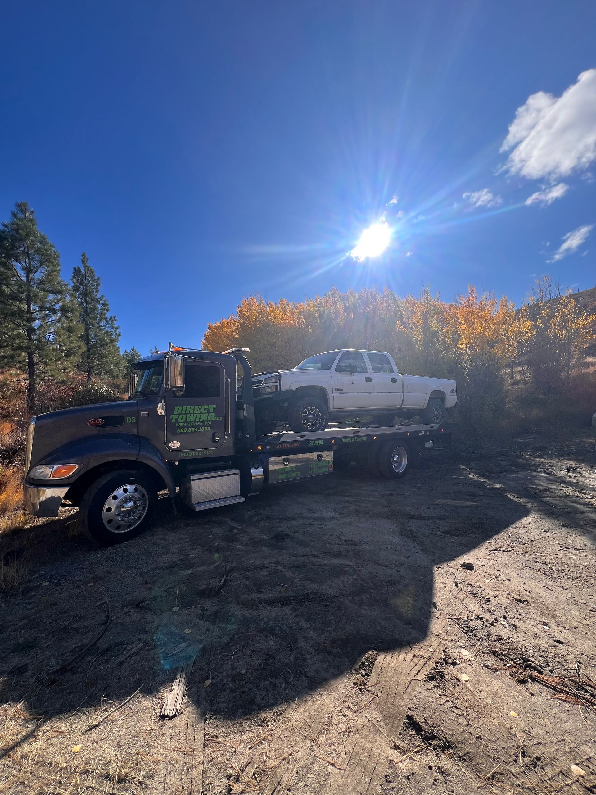 Truck towing a white pickup on a gravel road under a bright blue sky