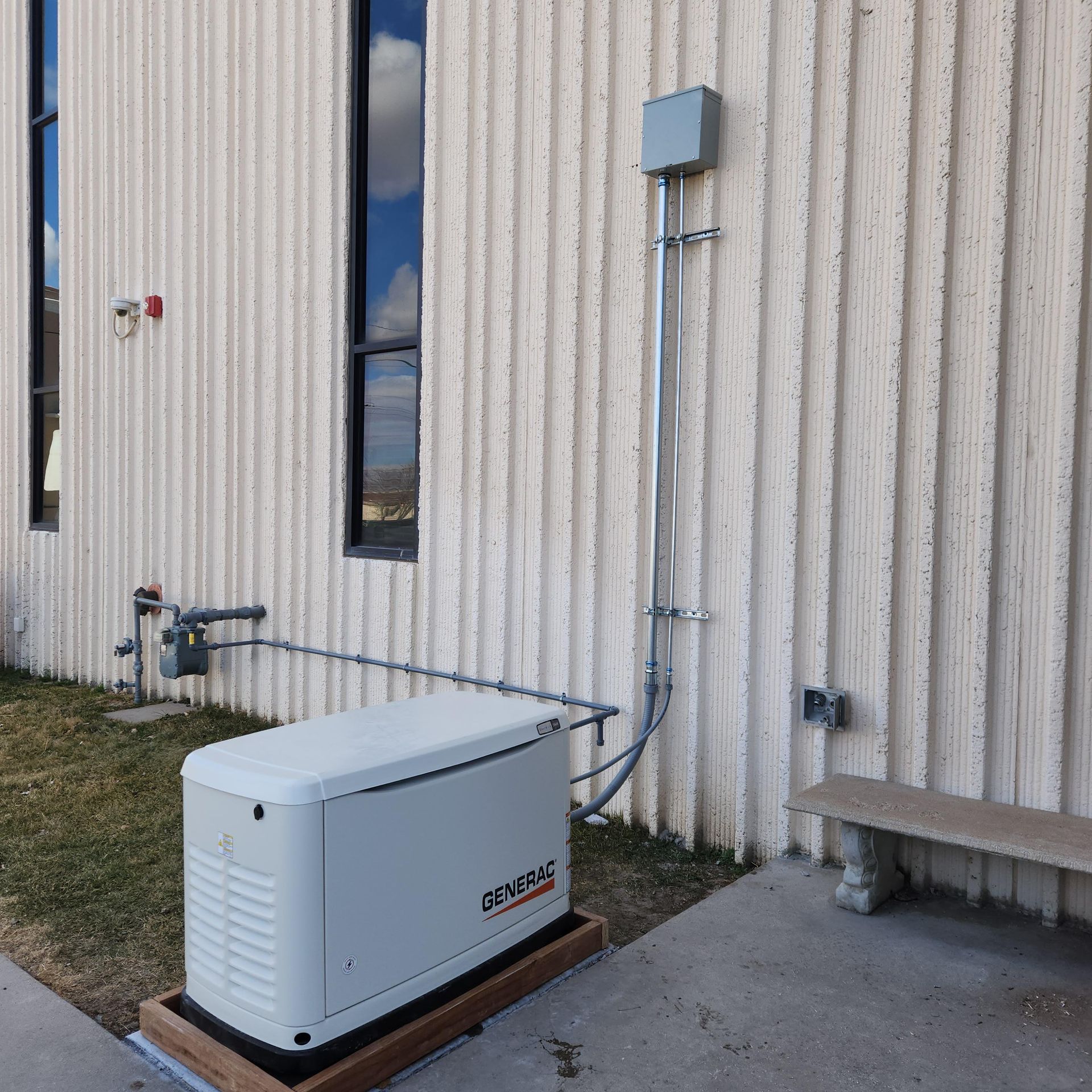 A generator is sitting outside of a building next to a bench